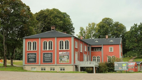 Ett rött hus vid en gräsplan, gröna träd i bakgrunden