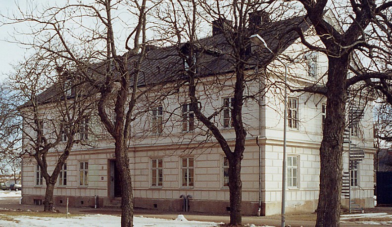 vitmålad putsad byggnad bakom en allé vintertid