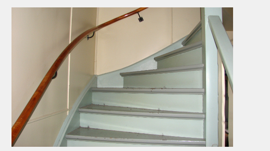 Trätrappa i grå linoljefärg med lackad träledstång och gulmålade väggar av masonitskivor