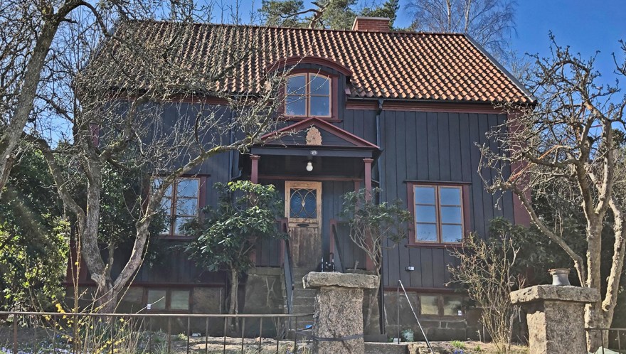 En envånings äldre villa med rött tegeltak och brun träpanel.