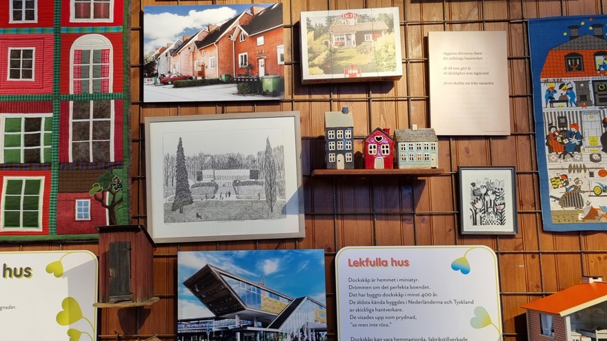 En vägg med ett kollage av tavlor, bonader och miniatyrer av hus.
