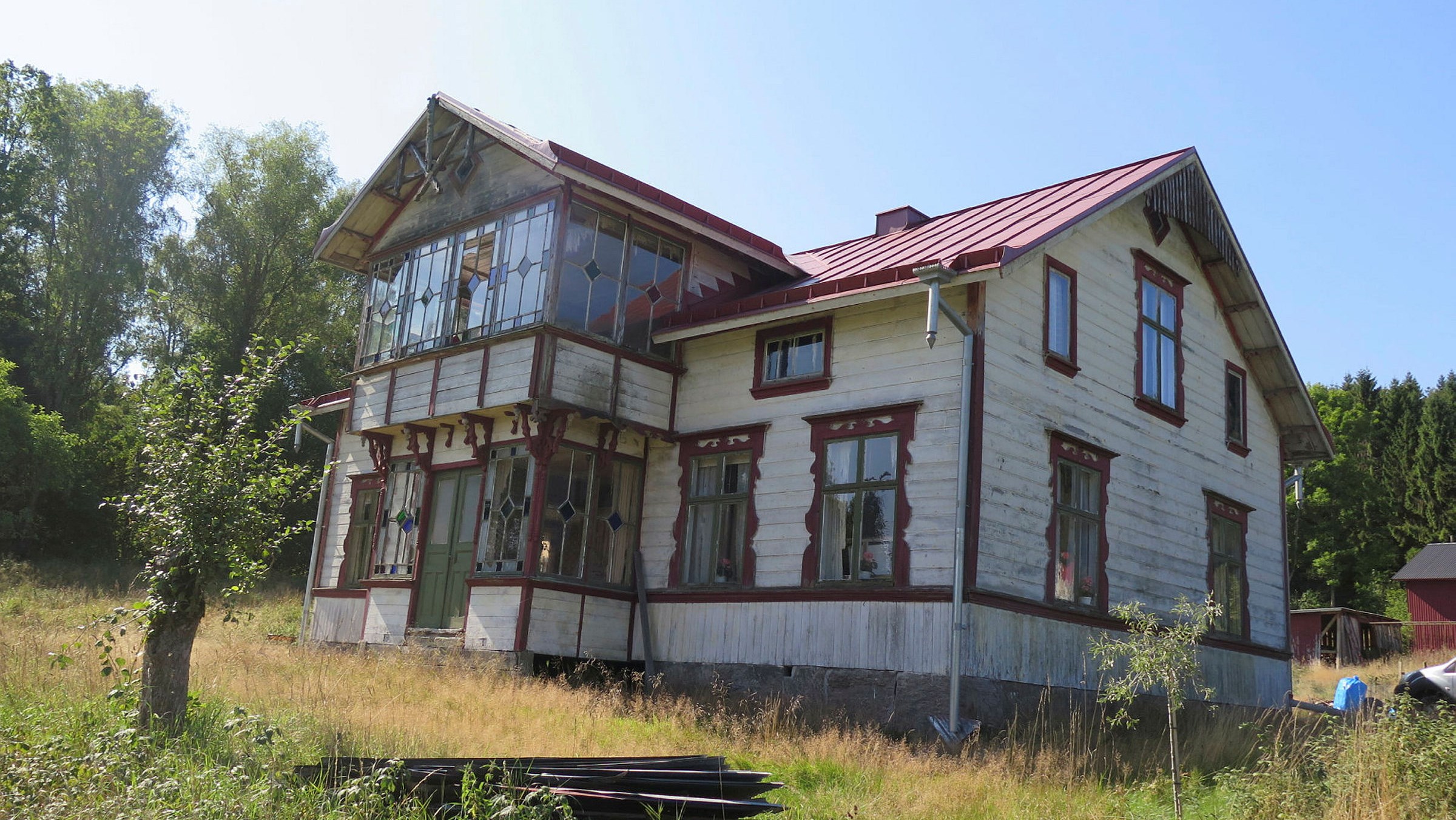 vacker sommardag en äng med ett stort slitet hus centralt i bild