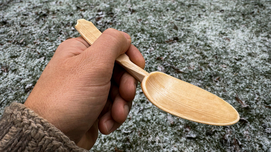 En hand håller en svängd sked av trä