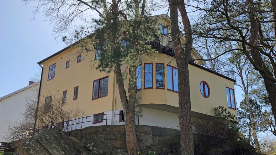 Putsad byggnad i gult vilande på berg och en hög stengrund