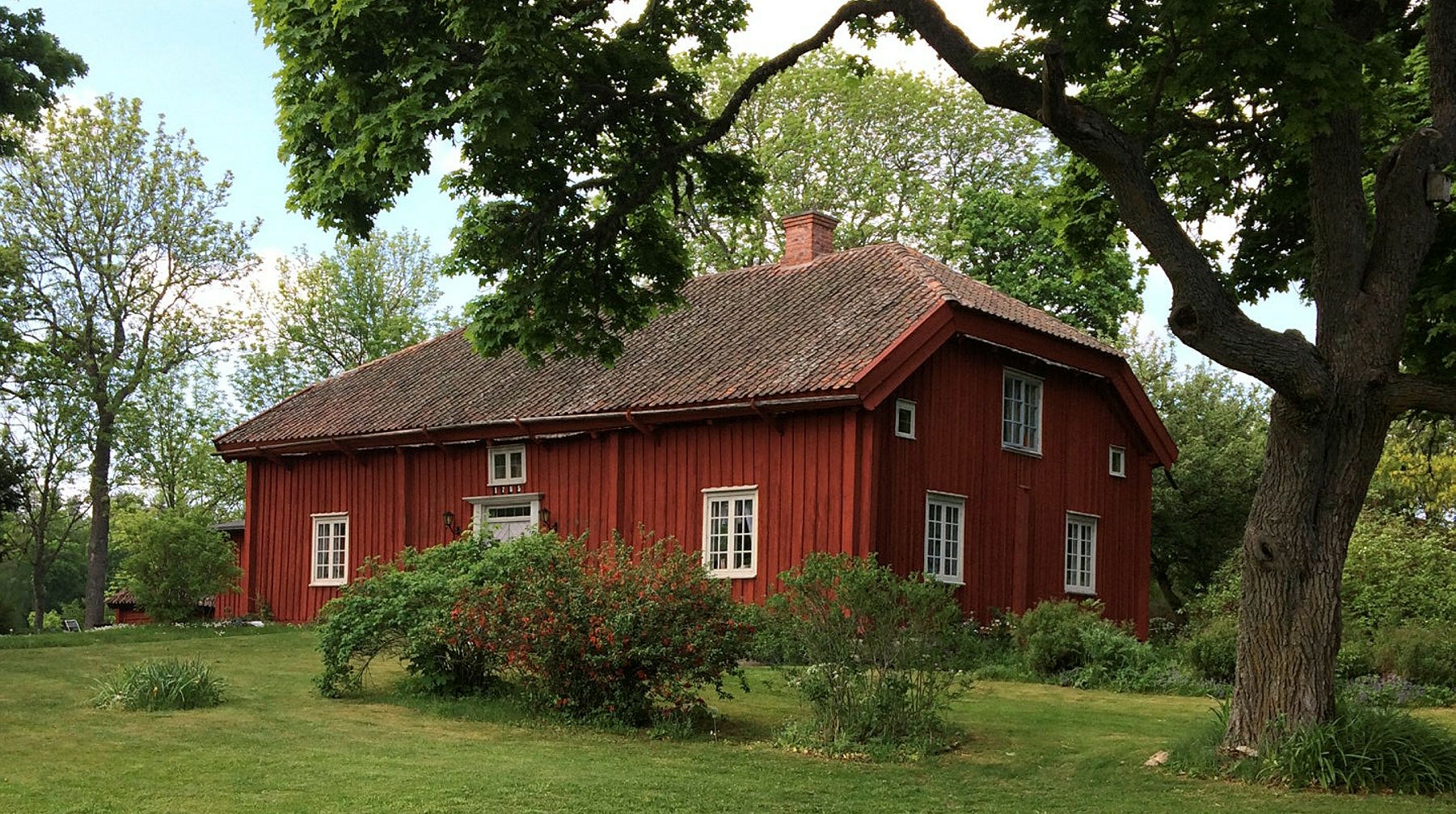 En röd stuga med valmat tak i gröna omgivningar