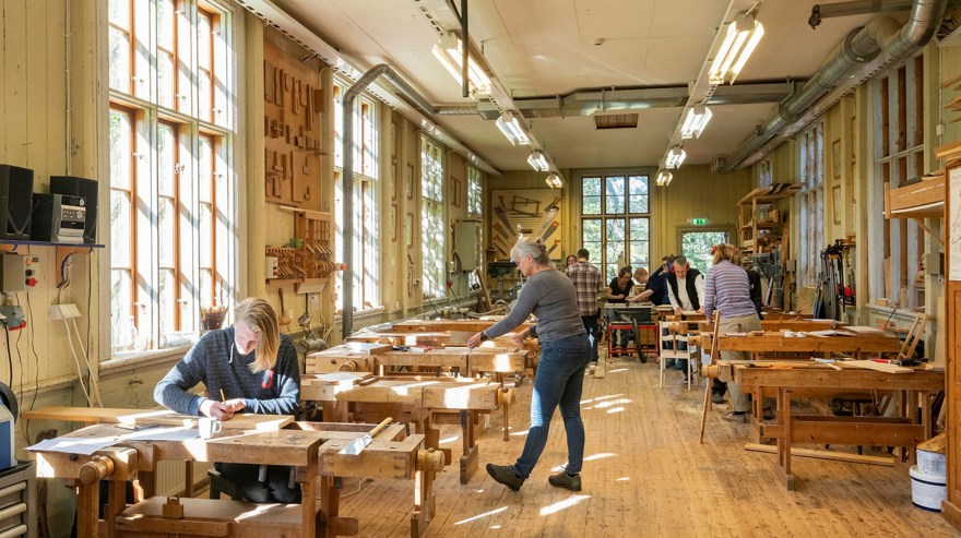 Ett långt rum med snickarbänkar och några personer som jobbar vid borden. Höga fönster på rummets långsidor.