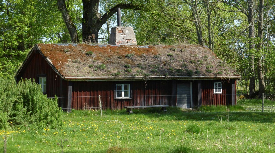 Ett lågt rött hus med mörkgrå knutlådor och torvtak