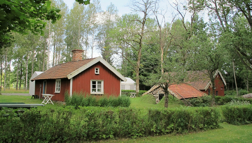 En torpmiljö med röda låga byggnader och växtlighet runtom.