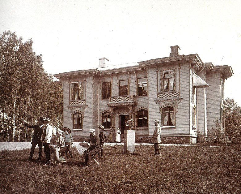 Gammalt foto i svartvitt på huset med flera personer på gräsmattan framför
