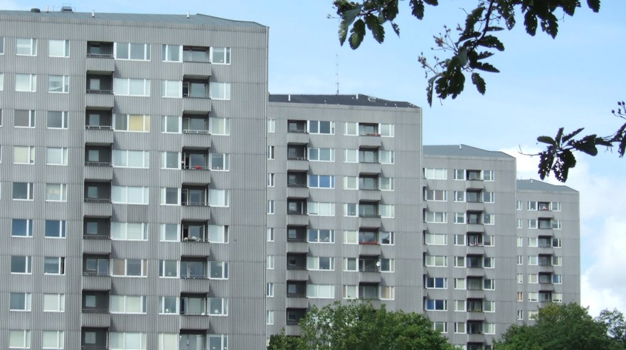 Grå flerfamiljshus står i rad med grönska omkring