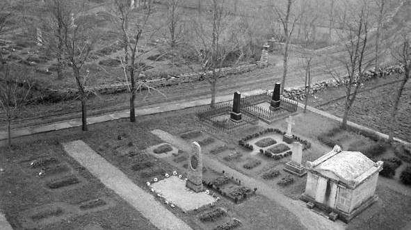 Svartvitt foto över vy av kyrkogård med påkostade gravmonument blandade med avlånga högar