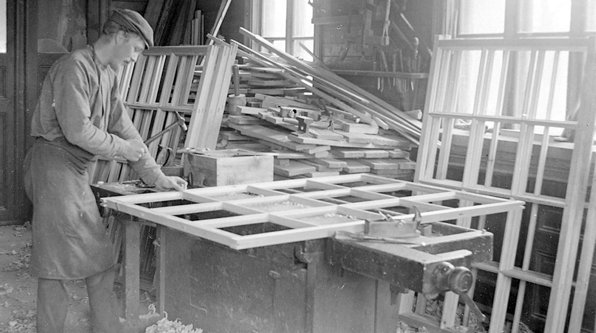 svartvitt foto med en man som bygger ett stort spröjsat fönster i en verkstad