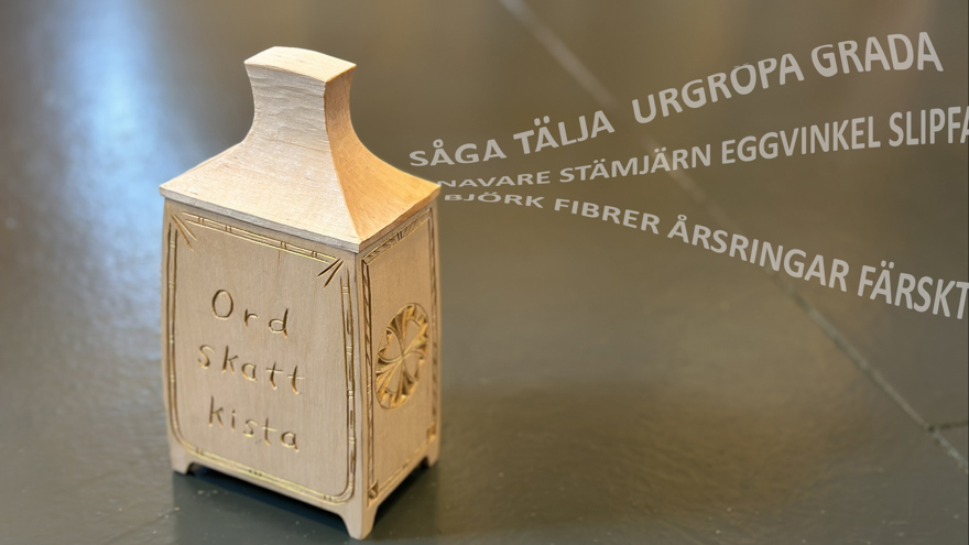 Ett ljust träskrin med skuren text "ordskattkista". En ström av slöjdrelaterade ord svävar ur den.