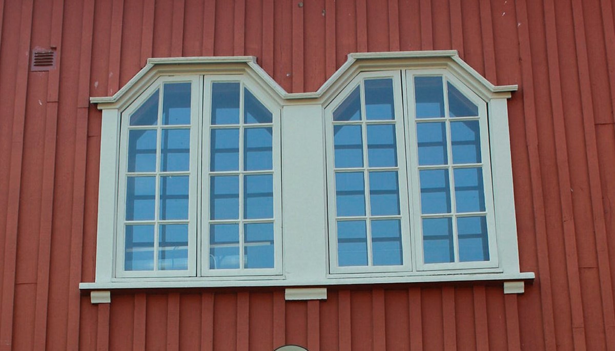 Två småspröjsade fönster målade i grått och den omgivande panelen är rödbrun