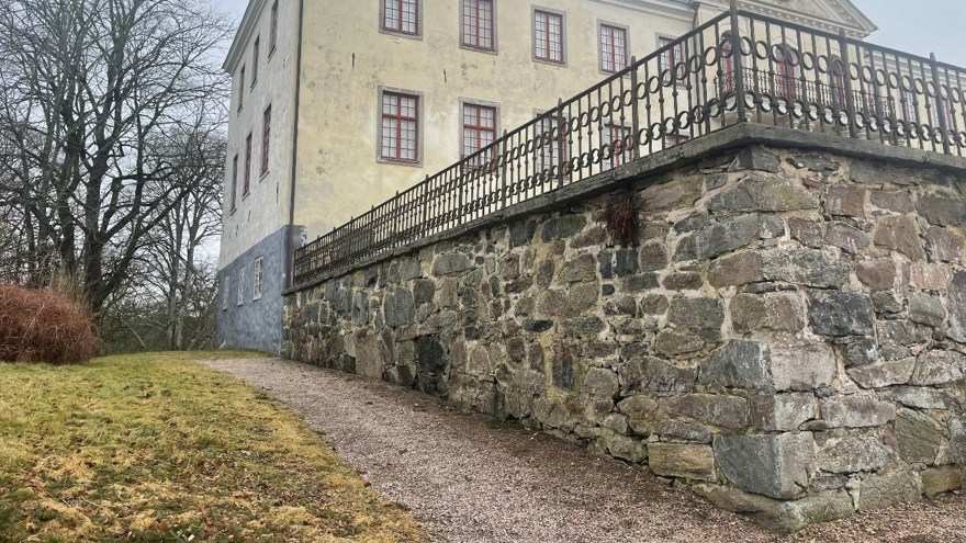 Bild på en naturstensmur framför en vit putsad äldre byggnad