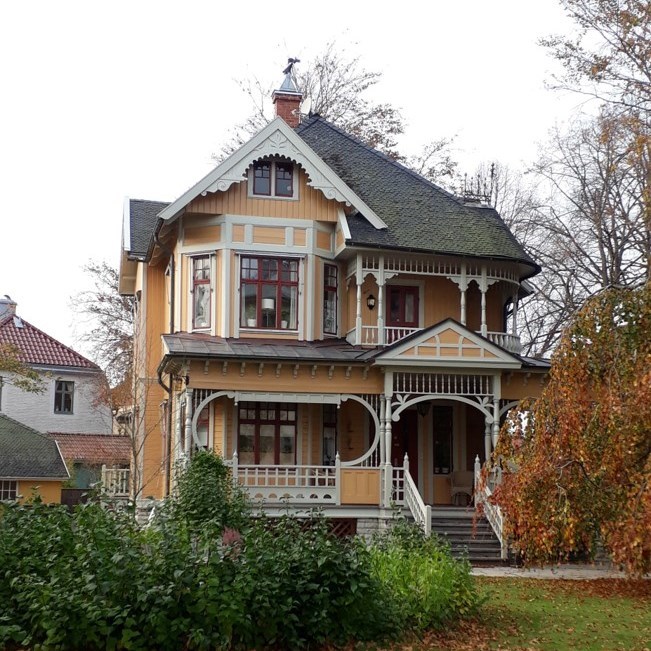 Högt gult hus med veranda med snickarglädje