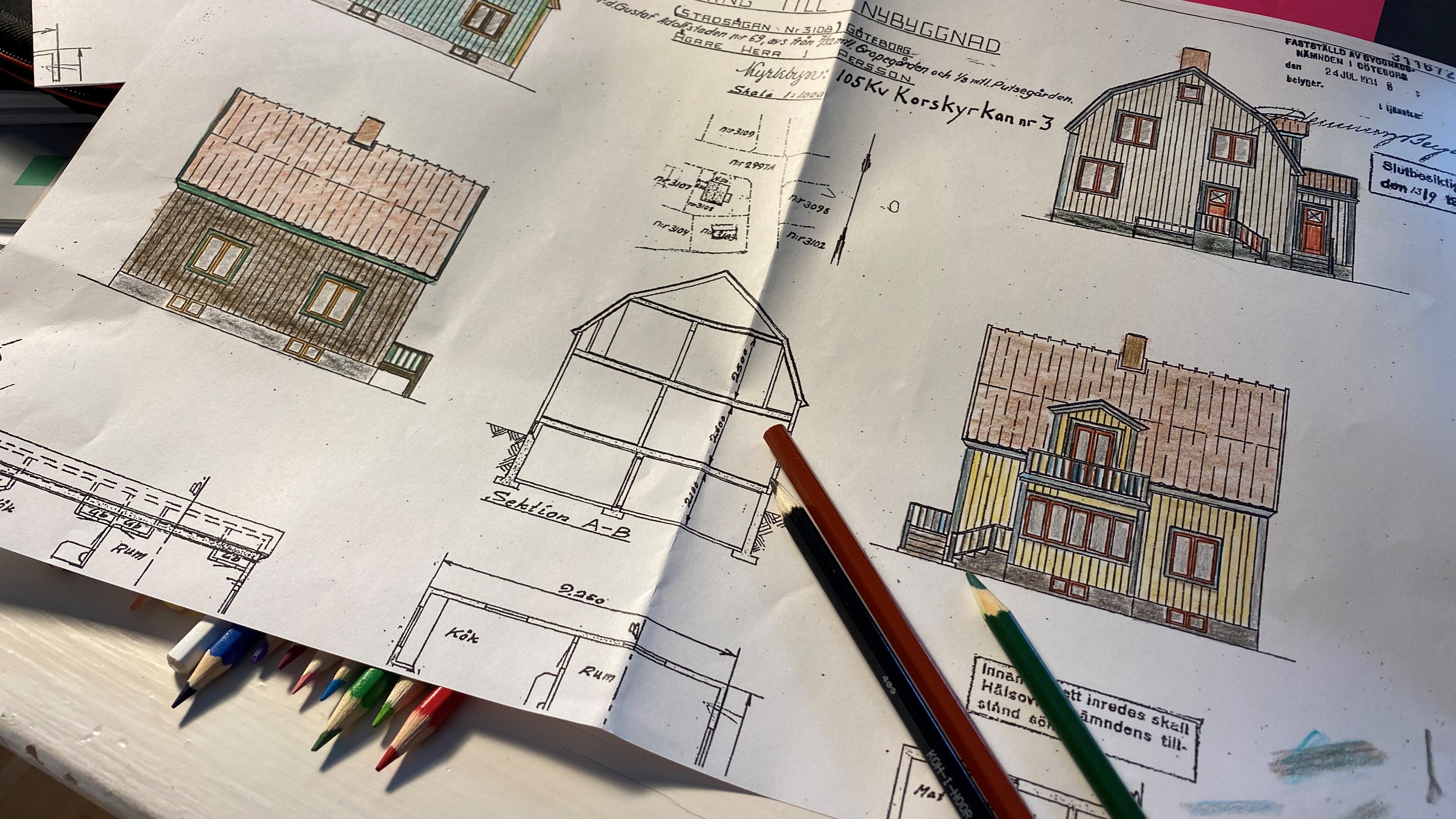En ritning på ett hus med fyra olika färgsättningar ritade med färgpennor. Pennor ligger på och under ritningen.