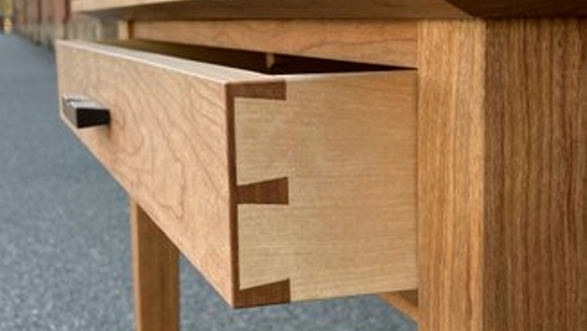 Ett skrivbord av trä med en halvt utrdragen skrivbordslåda med laxstjärtar (sinkningar) i hörnet.