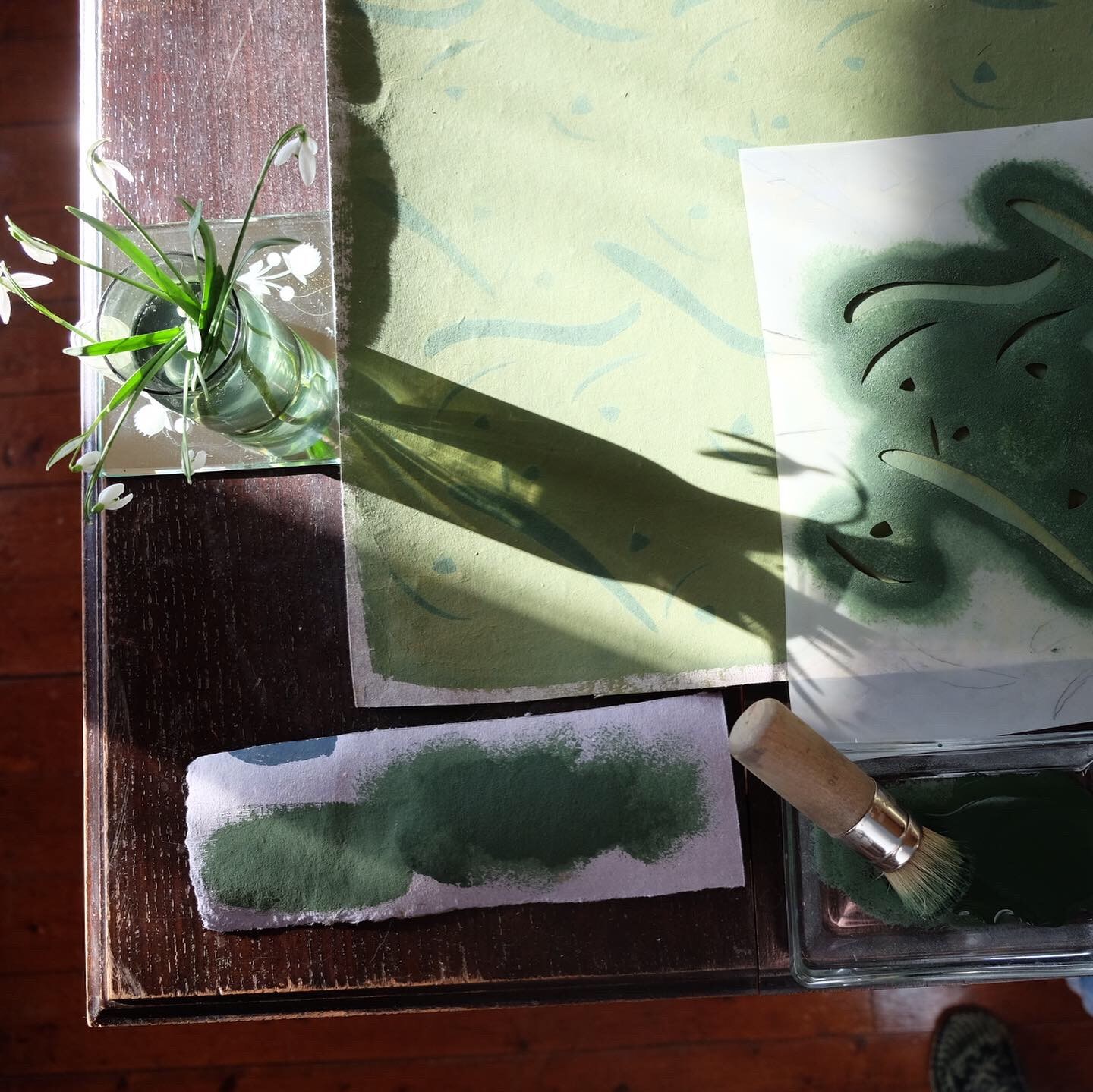 En solbelyst bordsskiva med schablonpensel och schablon på en påbörjad målad yta i grön