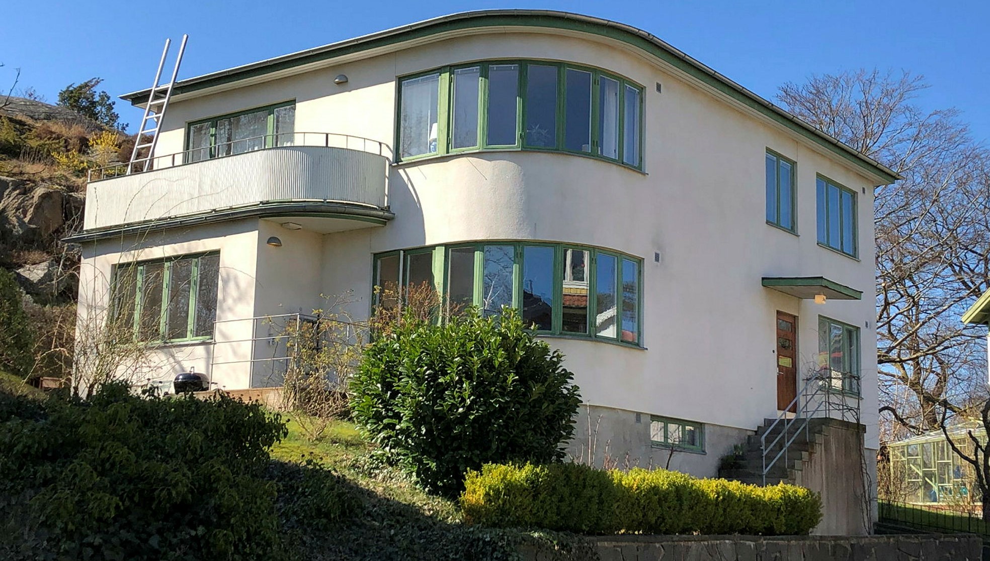En stor vit villa i vit putsad fasad och gröna fönster.