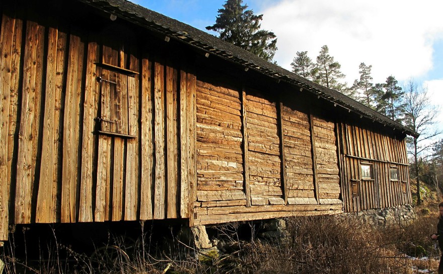 En lång ladugråd med stående panel och fackverk stående i gles skog