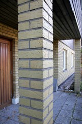 Detalj över en av två pelare som bär upp balkongen över entrépartiet. Pelarna är fyrkantiga och murade av samma gula tegel som byggnadens fasad.