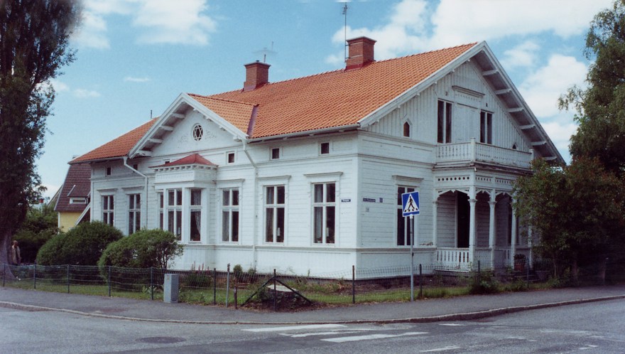 Ett stort hus med vitmålad snickarglädje och rött tak