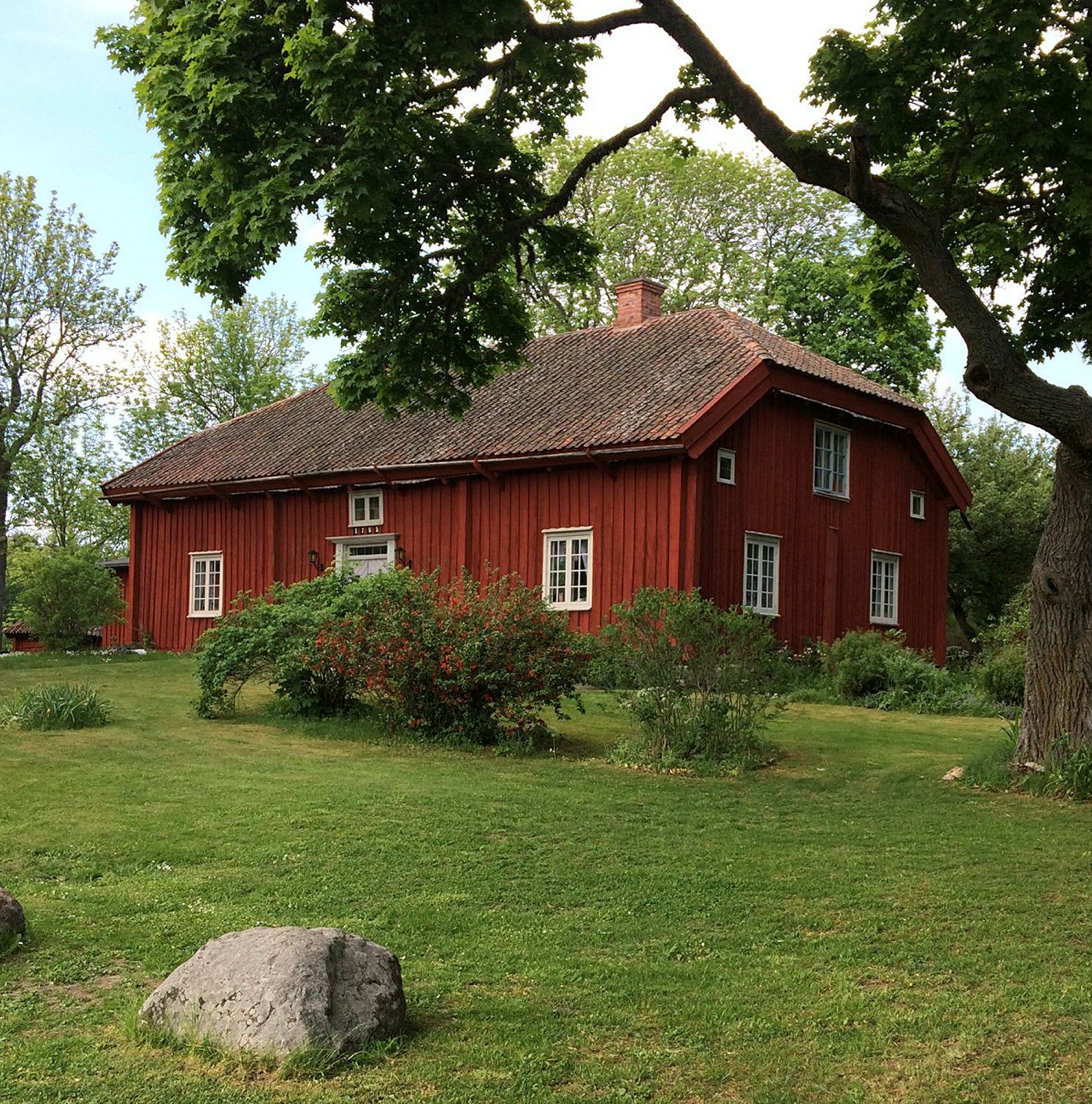 Röd stuga med rött tegeltak och vita fönster.