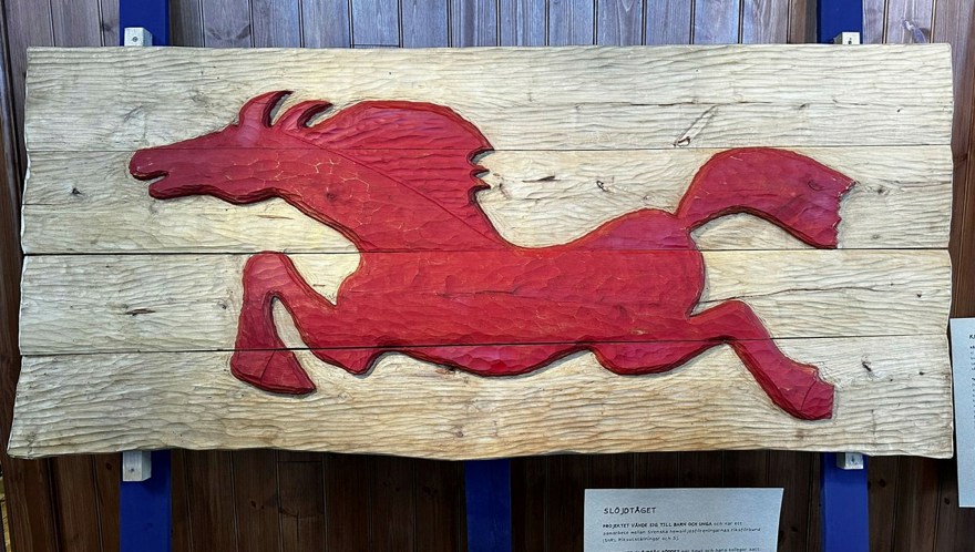 En skiva av brädor dekorerad med en skuren, röd, springande häst.