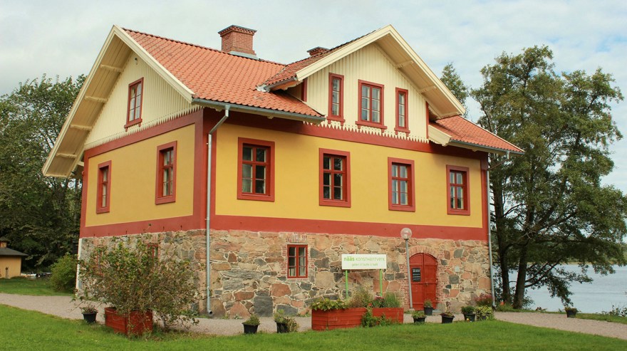 Ett putsat hus med stark gul kulör på fasad med röda detaljer och trävåning i ljusgult