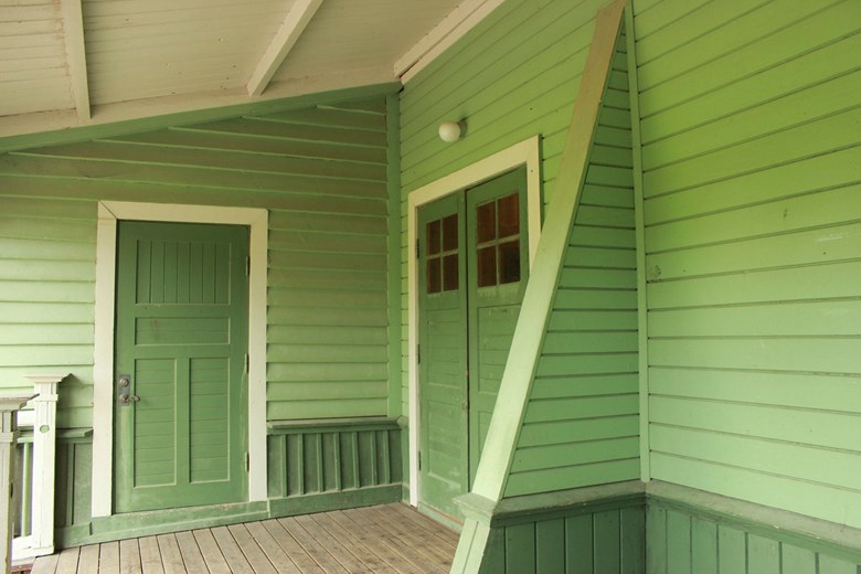 Insida av veranda med liggande panel och en låg bröstning med stående panel. Dörrar och låga bröstningen är målad i mörkt grön. Liggande panelen målad i ljust grönt.