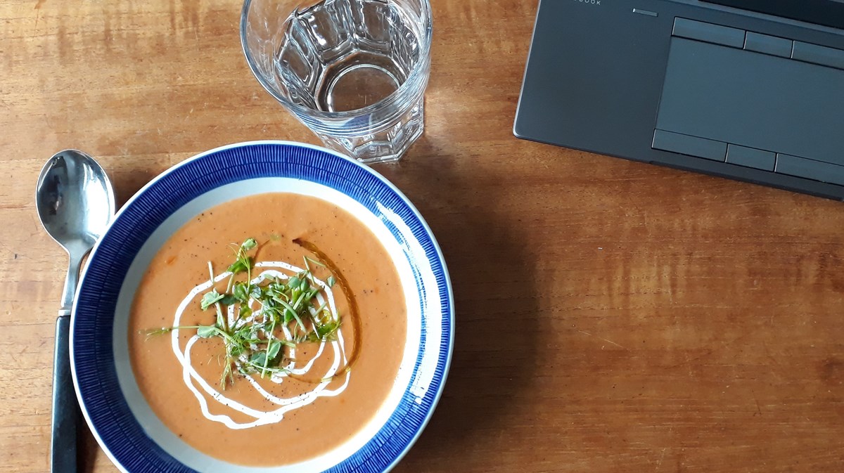 En skål med soppa och en laptop på ett träbord.