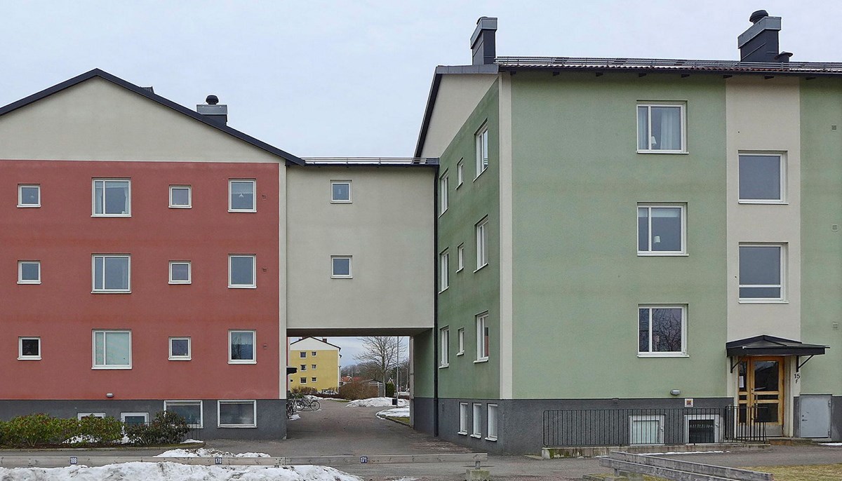 Ett putsat flerfamiljshus med flera sammanhängande byggnadskroppar målade i röda och gröna kulörer.