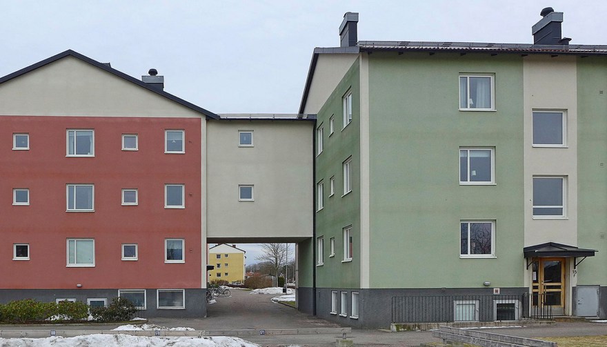 Ett putsat flerfamiljshus med flera sammanhängande byggnadskroppar målade i röda och gröna kulörer.