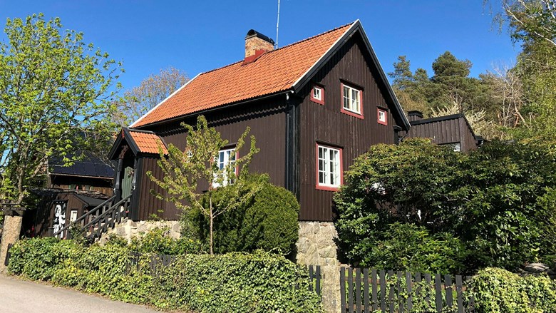 En villa med brun och svartmålad träpanel och rött tak, till vänster i bild är en entré med tegeltäckt vindskydd
