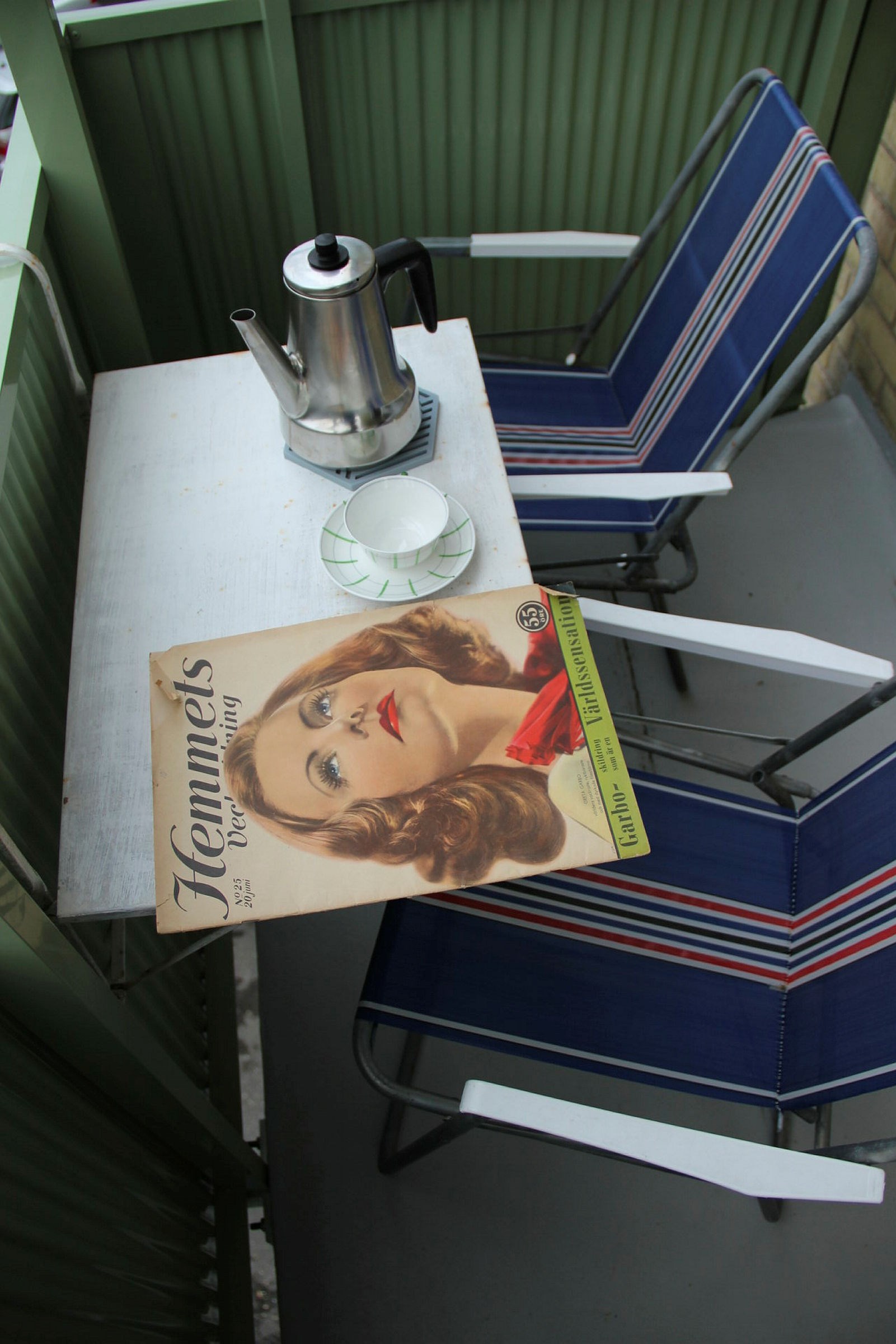 En balkong med två stolar och ett bord med tidning, kaffekopp och -termos.