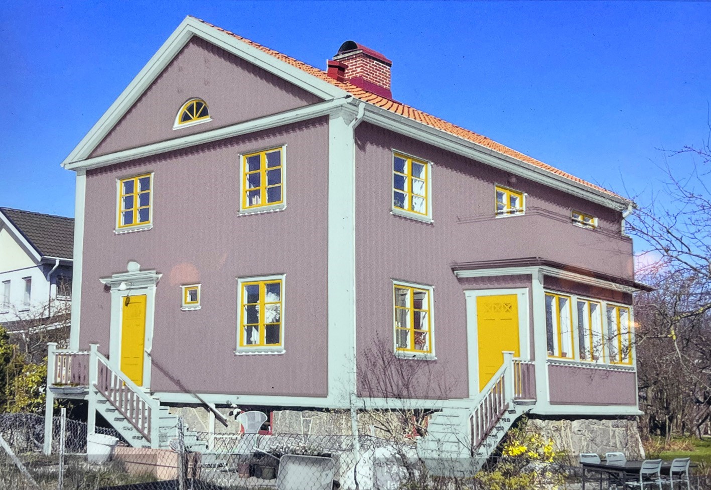 Brunt hus med grå foder och gula fönster.