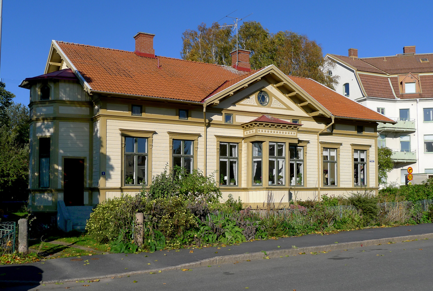 Ett stort gult hus med rött tak, ljusbruna snickerier och gröna fönster